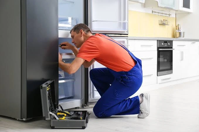 Technician in orange and blue workwear inspecting a refrigerator