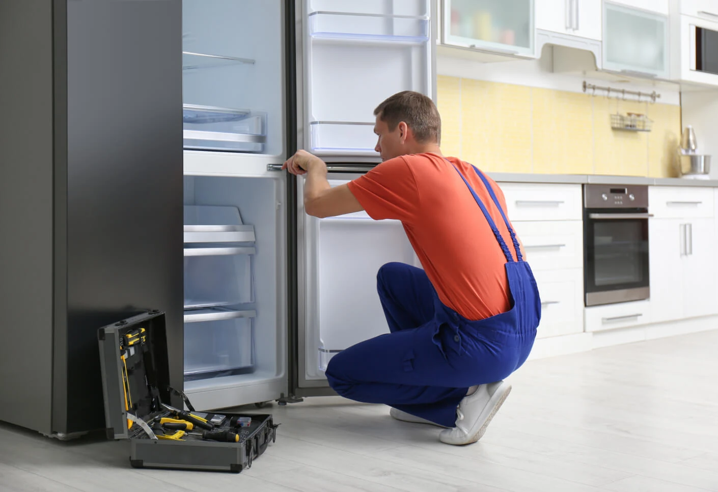 Technician inspecting an open refrigerator in a home kitchen